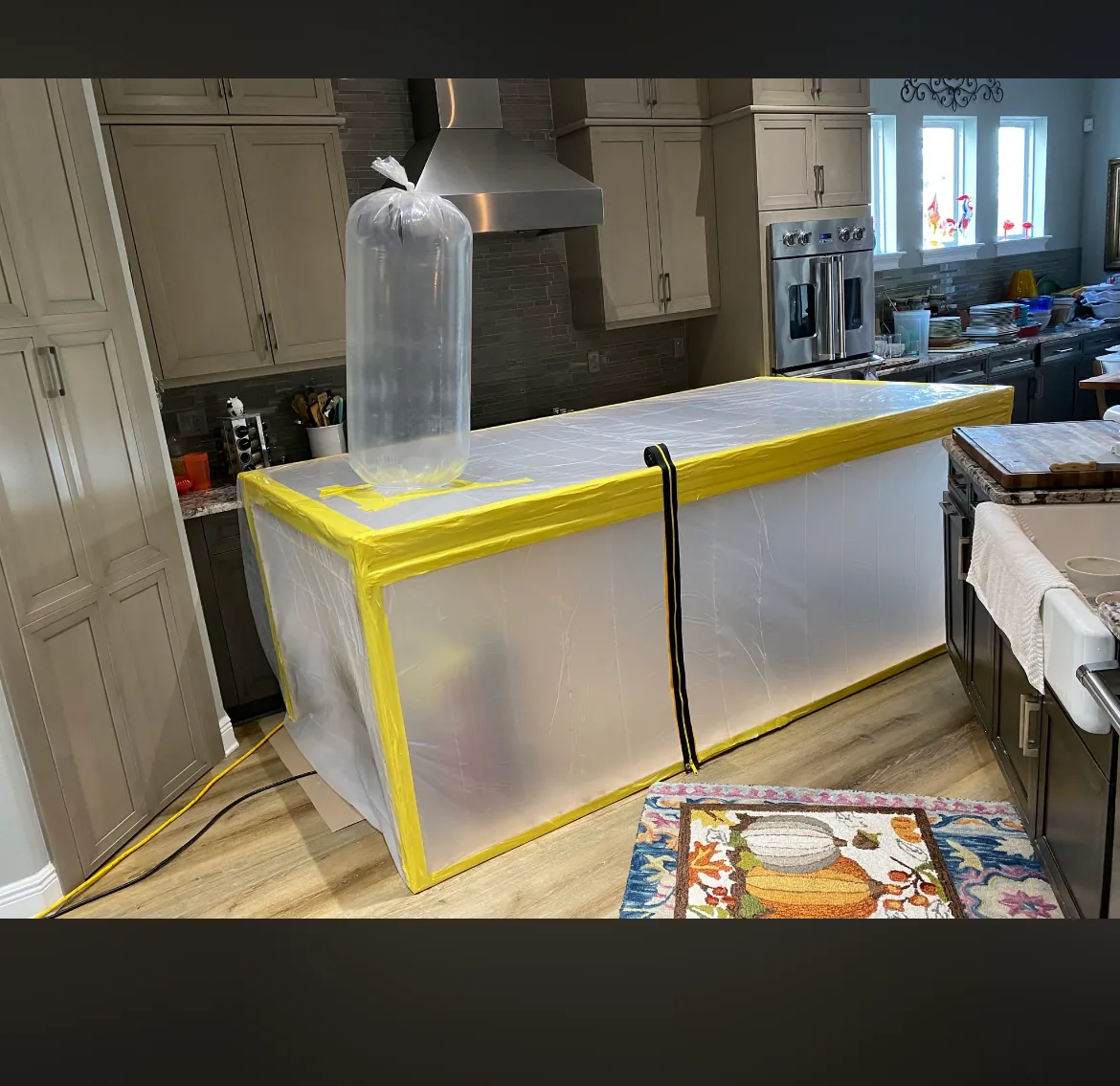 Kitchen island wrapped in clear plastic with yellow tape and a ventilation bag on top