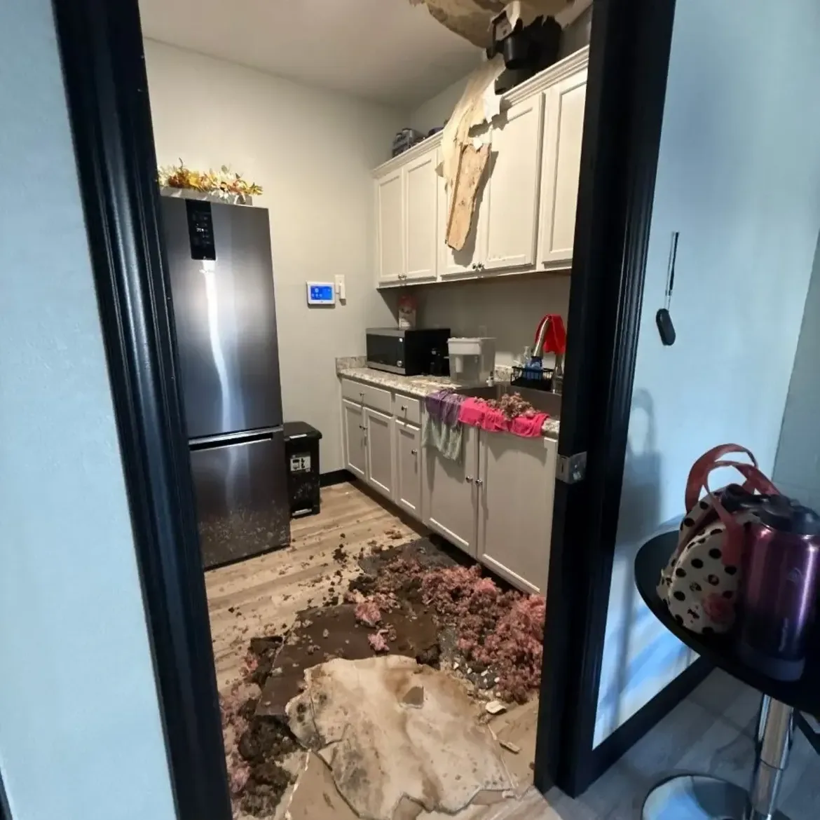 Small kitchen with a collapsed ceiling section, pink insulation and debris on the floor